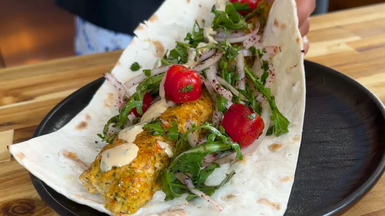 Plate with grilled chicken kebab fresh greens, cherry tomatoes, and sauce on a wooden table, ready to eat.