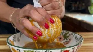 Hands squeezing veggies through cloth over floral bowl.