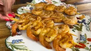 Grilled shrimp skewers on a floral plate, beautifully seasoned and ready to serve as a delicious seafood dish.