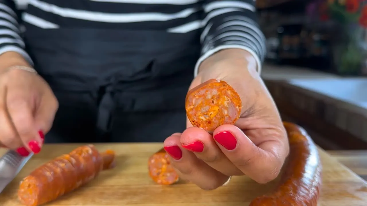 Person holding sliced chorizo on a cutting board, preparing food in a kitchen setting.