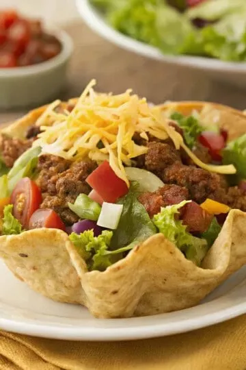 Delicious taco salad in a crispy tortilla bowl with ground beef, lettuce, tomatoes, and cheese, served on a white plate.