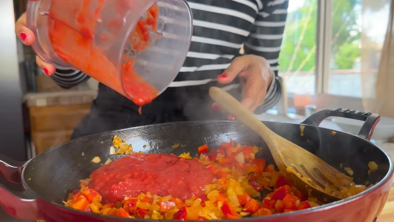 Person adding tomato sauce to skillet.