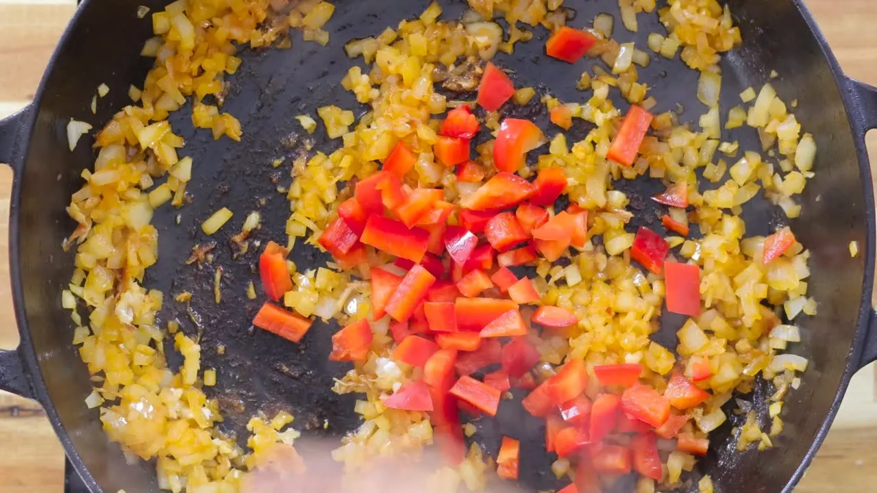 Diced onions and red peppers sautéing in a black skillet for a savory dish.