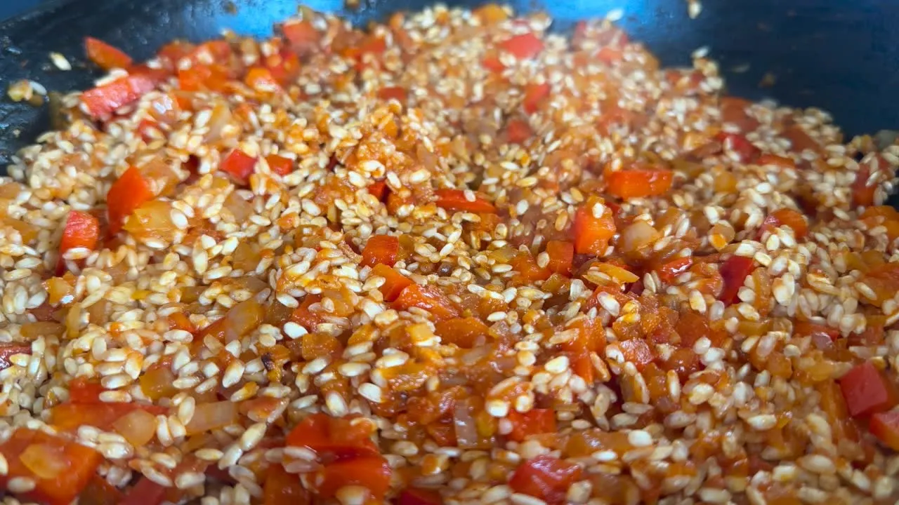 Close-up of a colorful risotto dish with red bell peppers and onions in a pan.