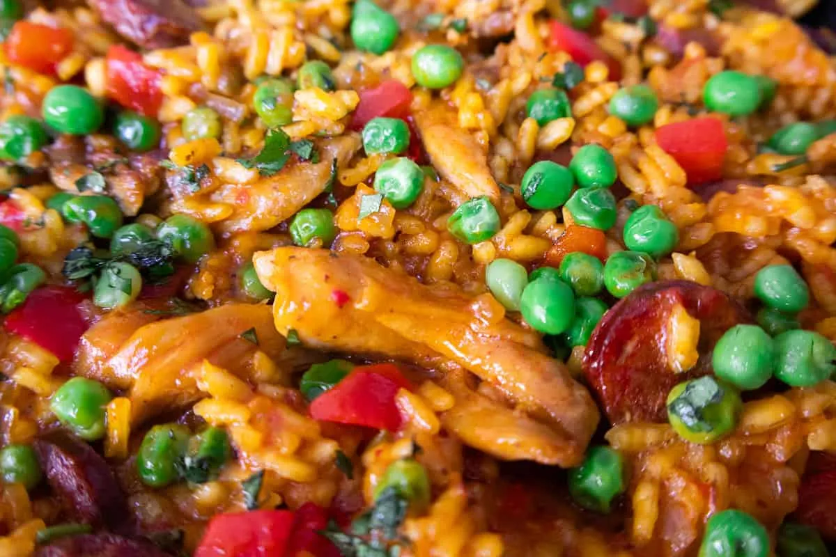 Close-up of flavorful chicken paella with peas, bell peppers, and chorizo, showcasing vibrant ingredients.