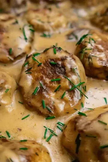 Savory smothered chicken meatballs garnished with fresh chives in rich gravy sauce, perfect for a hearty dinner.