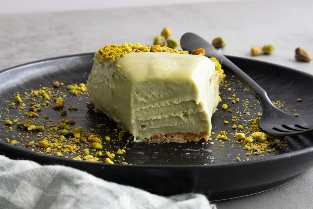 Slice of creamy No-Bake Mascarpone Pistachio Cheesecake on a black plate with scattered nuts.