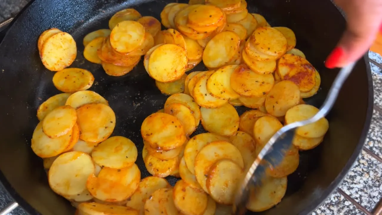 Golden fried potato slices in a skillet, being stirred with a fork.