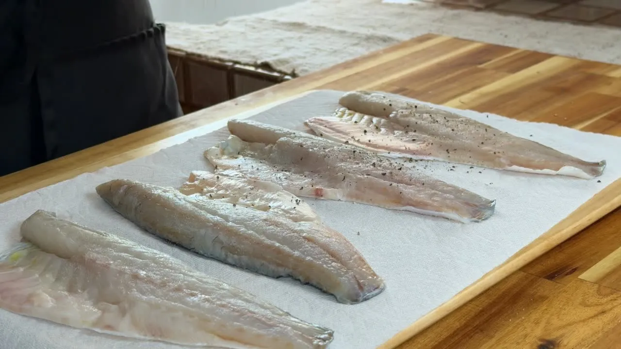 Fresh fish fillets on a wooden board, seasoned with black pepper.