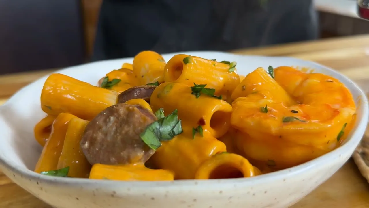 Creamy seafood rigatoni with shrimp and sausage, garnished with herbs in a white bowl.