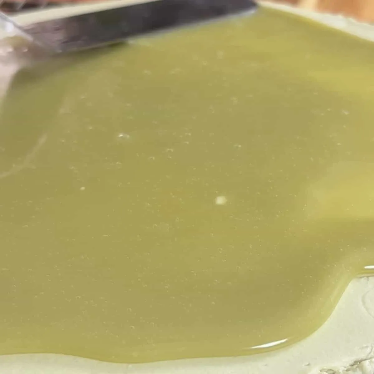 Close-up of fresh olive oil being spread with a knife on a light surface.