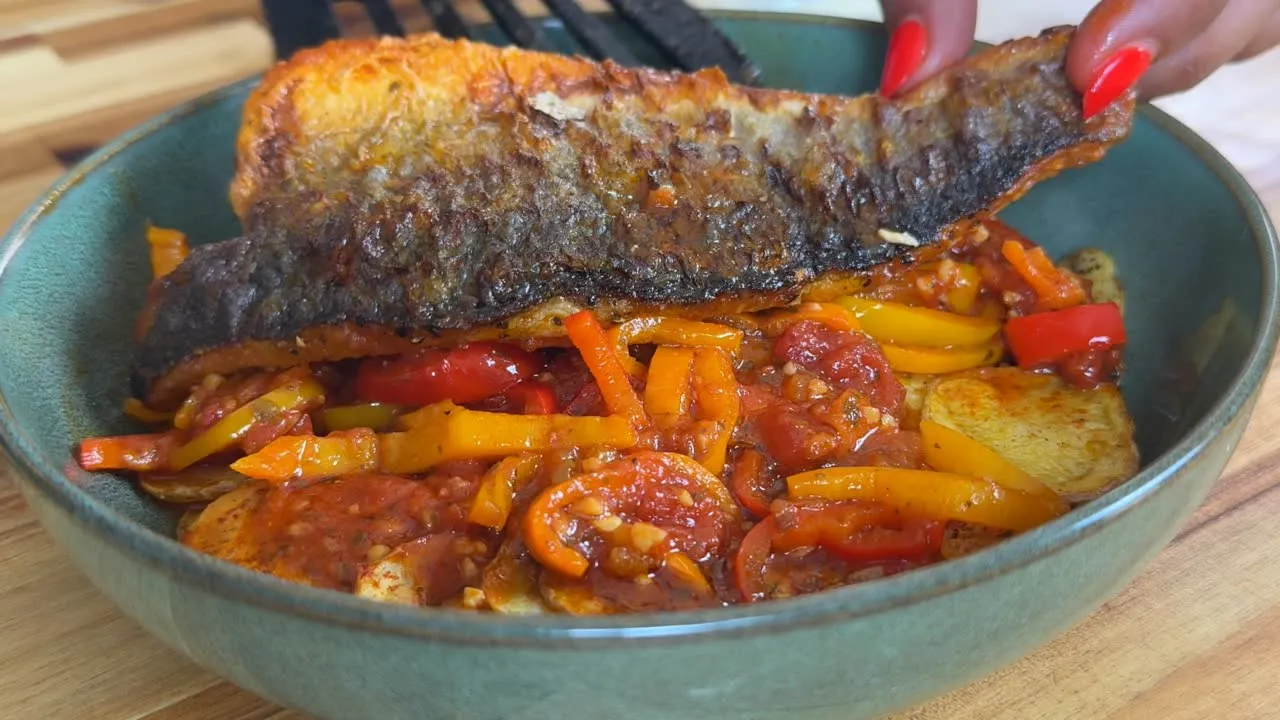 Grilled fish with crispy skin on roasted peppers and tomato sauce in a green bowl.
