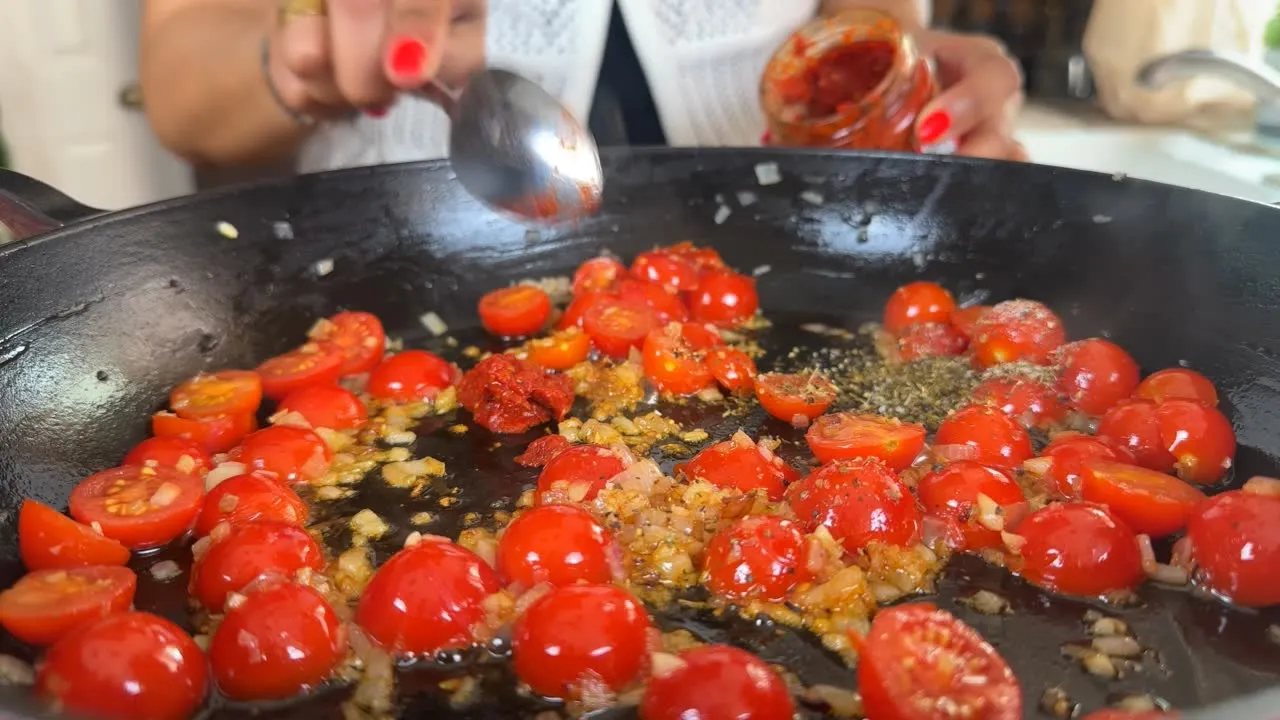 Cooking cherry tomatoes and onions in a pan with spices, being stirred with a spoon.