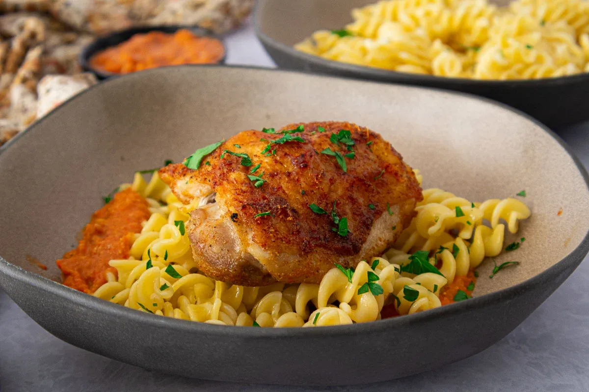 Crispy chicken romesco with fusilli pasta garnished with fresh parsley in a gray bowl.
