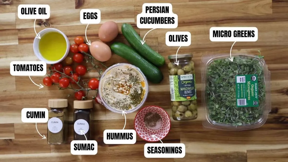 Assorted ingredients for Mediterranean Hummus Bowl: tomatoes, eggs, cucumbers, micro greens, spices, hummus, olives, olive oil.