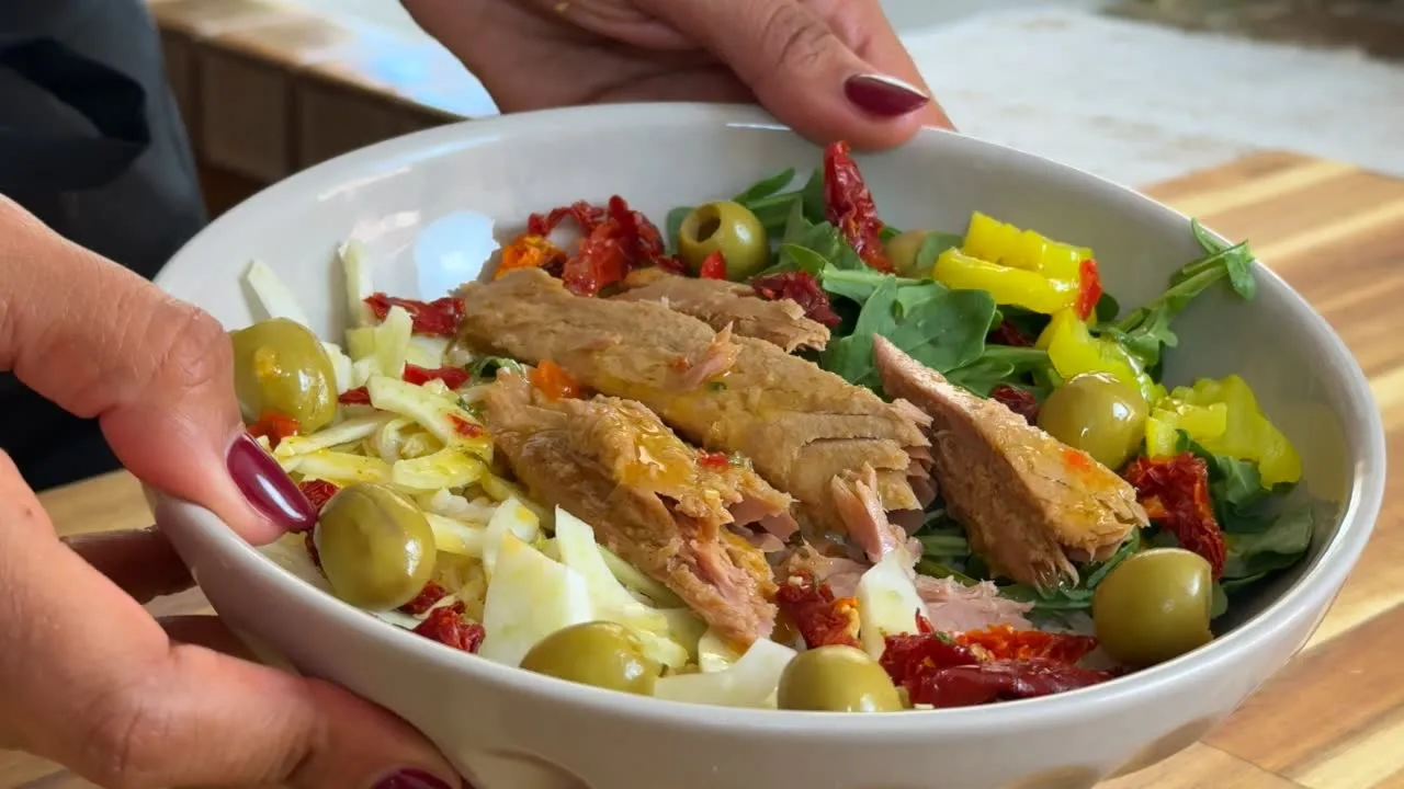 Fresh tuna salad with olives, sun-dried tomatoes, and greens in a white bowl.