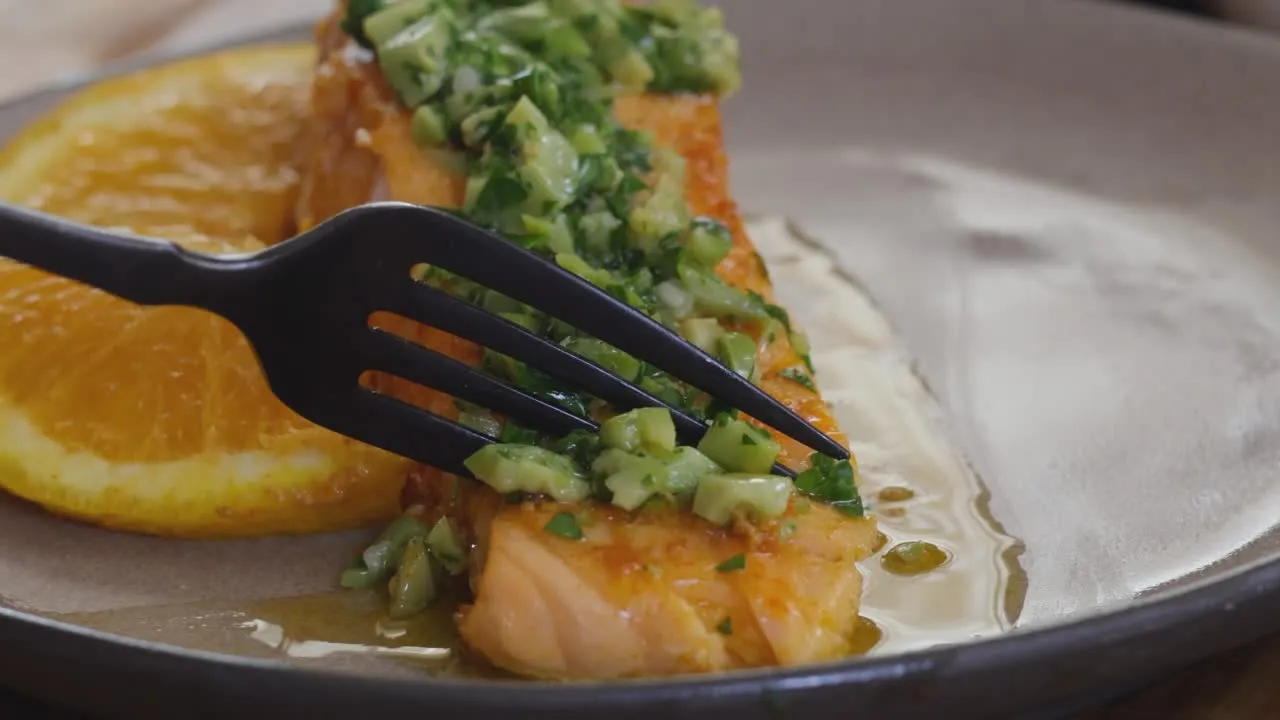 Grilled salmon with avocado salsa and orange slice on a plate with fork.