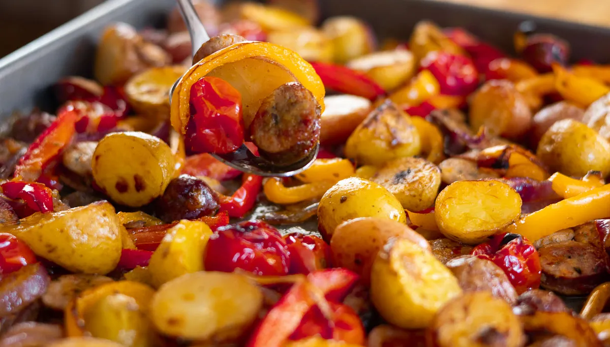 Sheet pan with roasted sausage, potatoes, and colorful bell peppers.