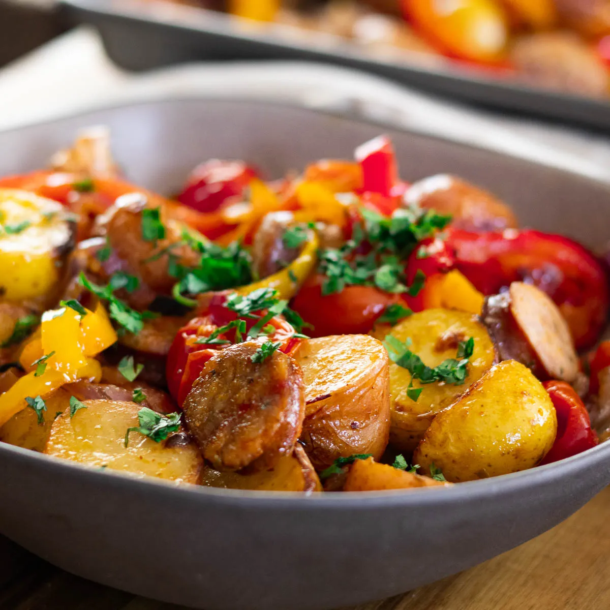 Delicious roasted sausage, peppers, and potatoes and herbs in a serving dish.