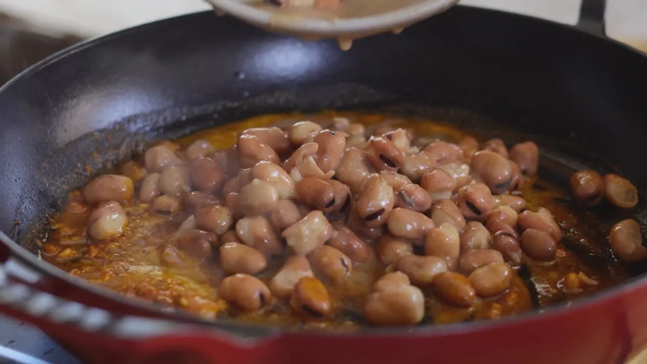 Cooking fava beans in a red skillet with seasoned sauce.