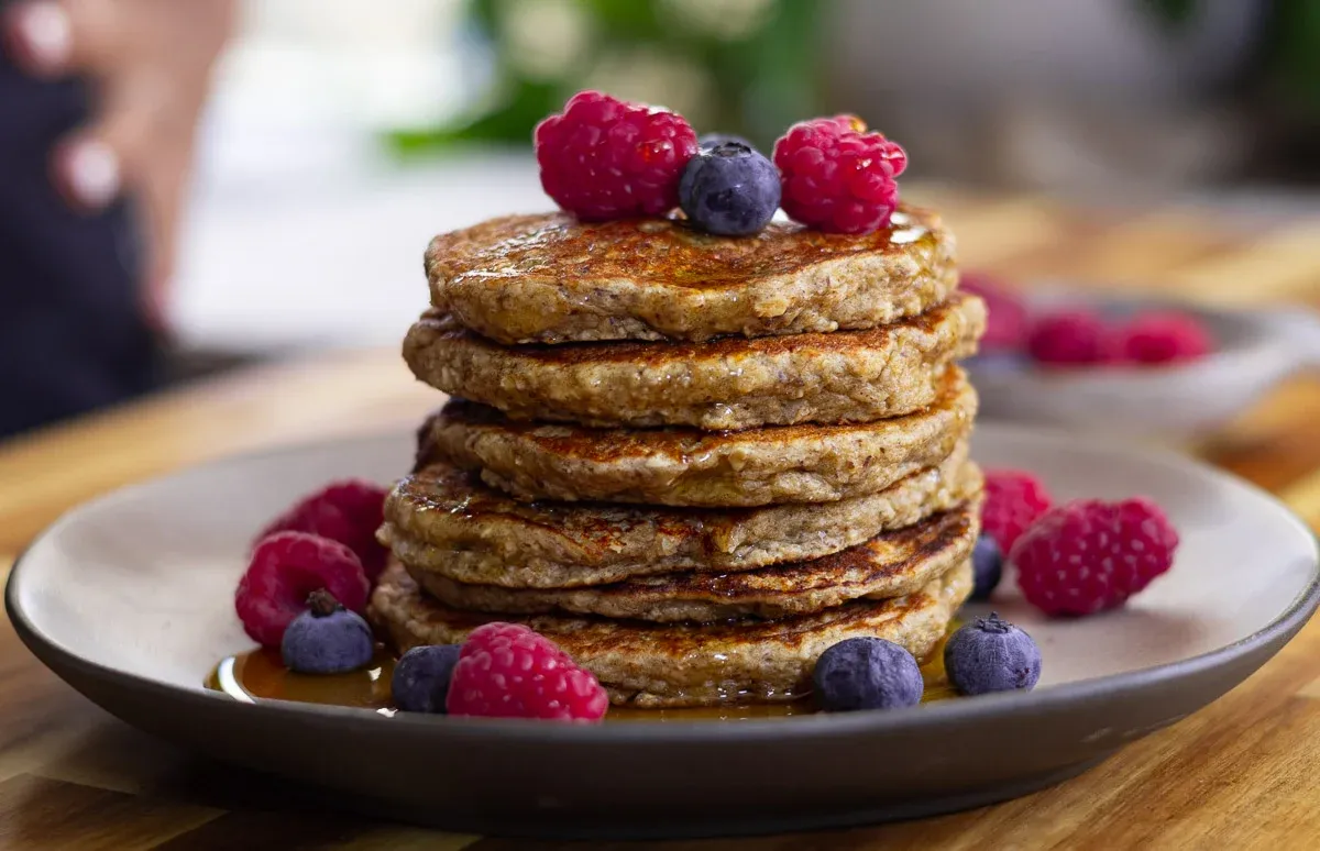Stack of pancakes topped with fresh raspberries and blueberries on a plate with syrup.
