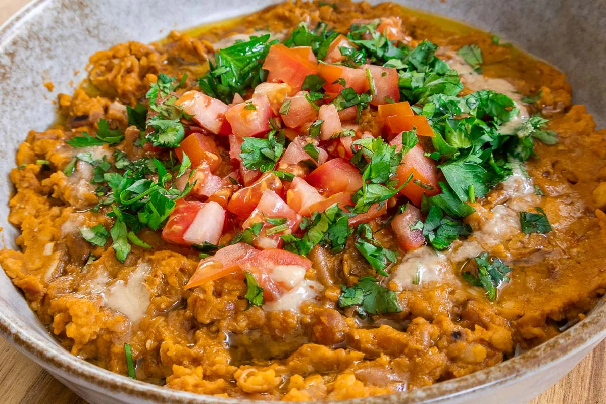 Creamy Ful Mudammas topped with diced tomatoes and fresh herbs in a bowl.