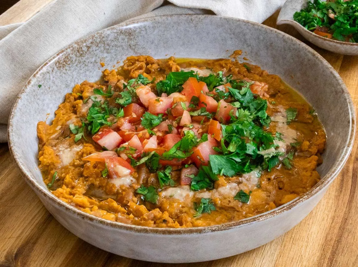 Ful mudammas topped with fresh diced tomatoes and parsley in a rustic bowl.