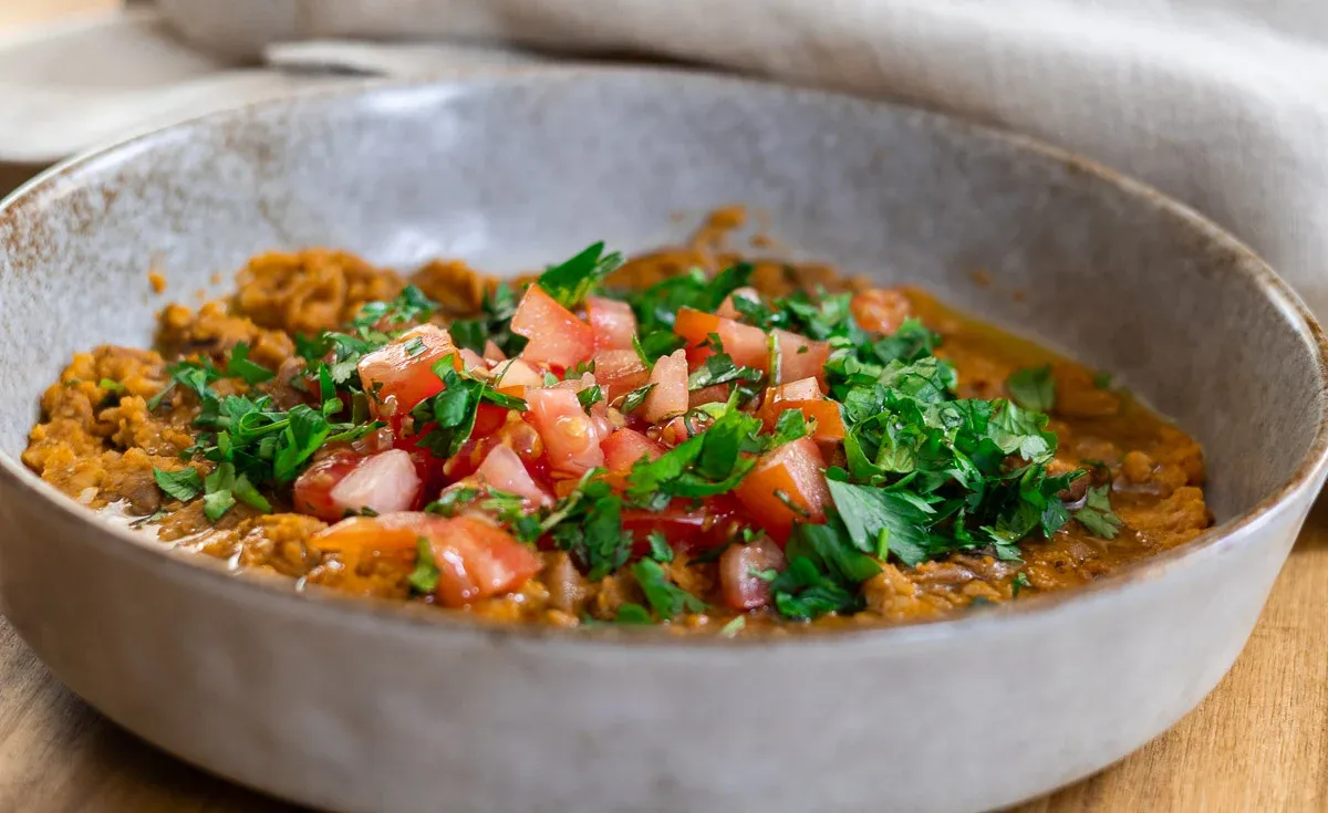 Delicious lentil stew topped with fresh tomatoes and parsley in a rustic bowl, perfect for a healthy meal.