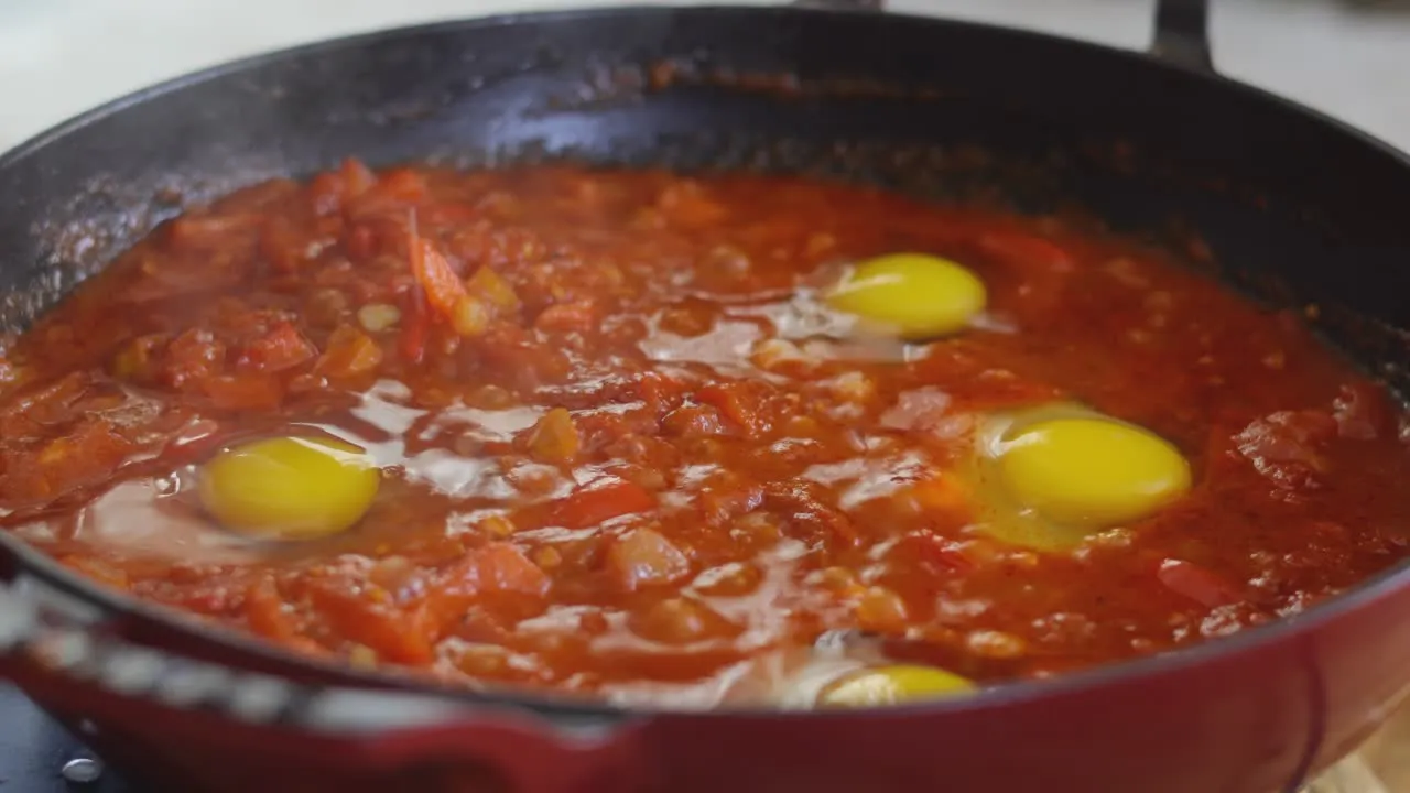 Shakshuka cooking in a pan with tomatoes and eggs simmering in rich red sauce.