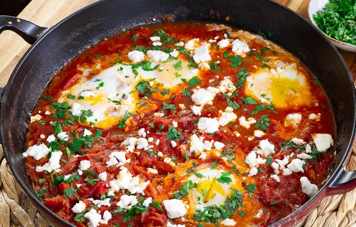 Savory Shakshuka in skillet with poached eggs, tomatoes, feta, and herbs.