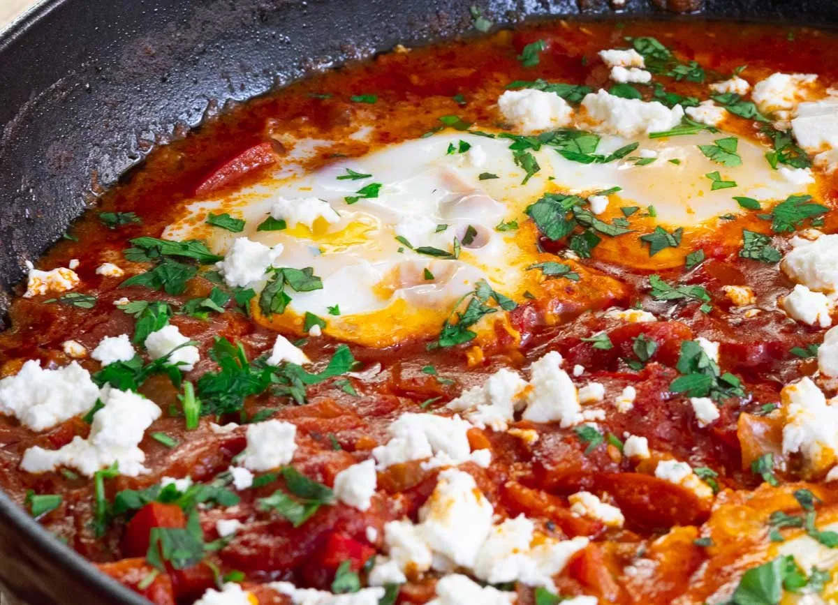 Delicious shakshuka with poached eggs, tomatoes, feta, and herbs in a skillet.