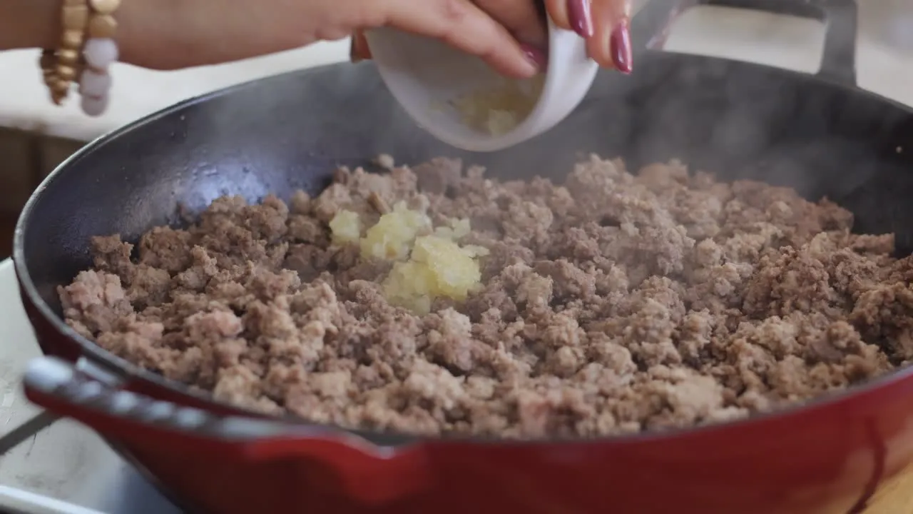 Adding garlic to ground meat in a red skillet.