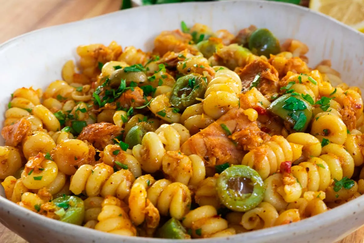 Delicious Creamy Calabrian Chili Tuna Pasta with olives, tuna, herbs, and spices in a white bowl.