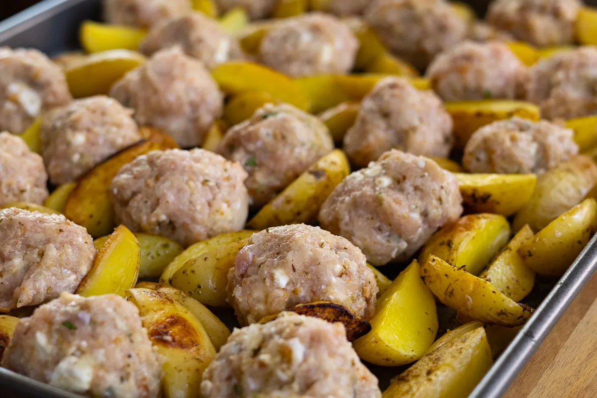 Baked meatballs with roasted potatoes on a baking tray, seasoned and ready to serve.