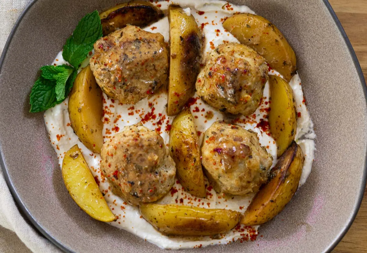 Greek chicken feta meatballs and roasted potatoes on whipped feta with herbs in a bowl.