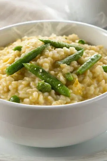 Risotto agli Asparagi (Asparagus Risotto) topped with fresh herbs served in a white bowl.