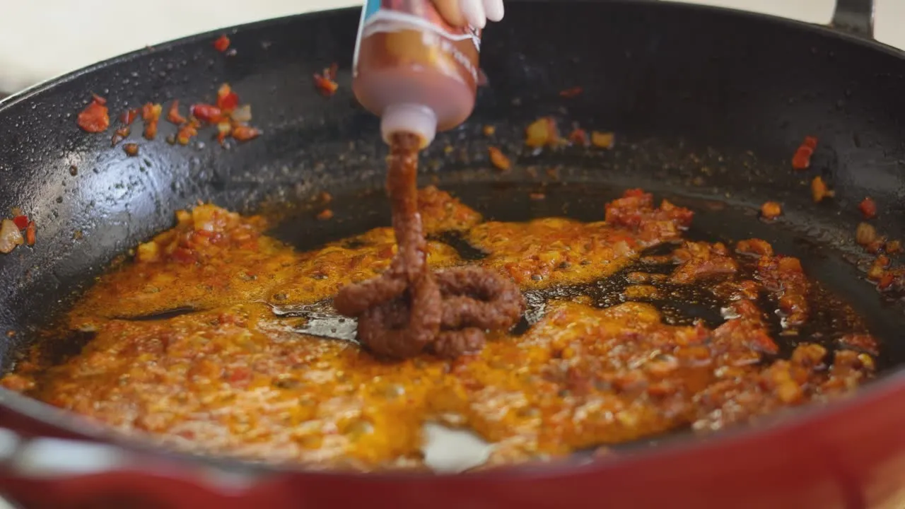 Adding tomato paste to a sizzling pan with spices and onions for a rich, flavorful sauce.