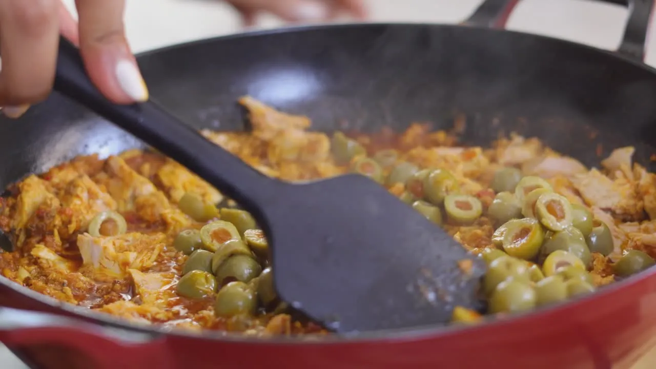 Cooking tuna with olives in a pan, stirred with a black spatula, close-up.