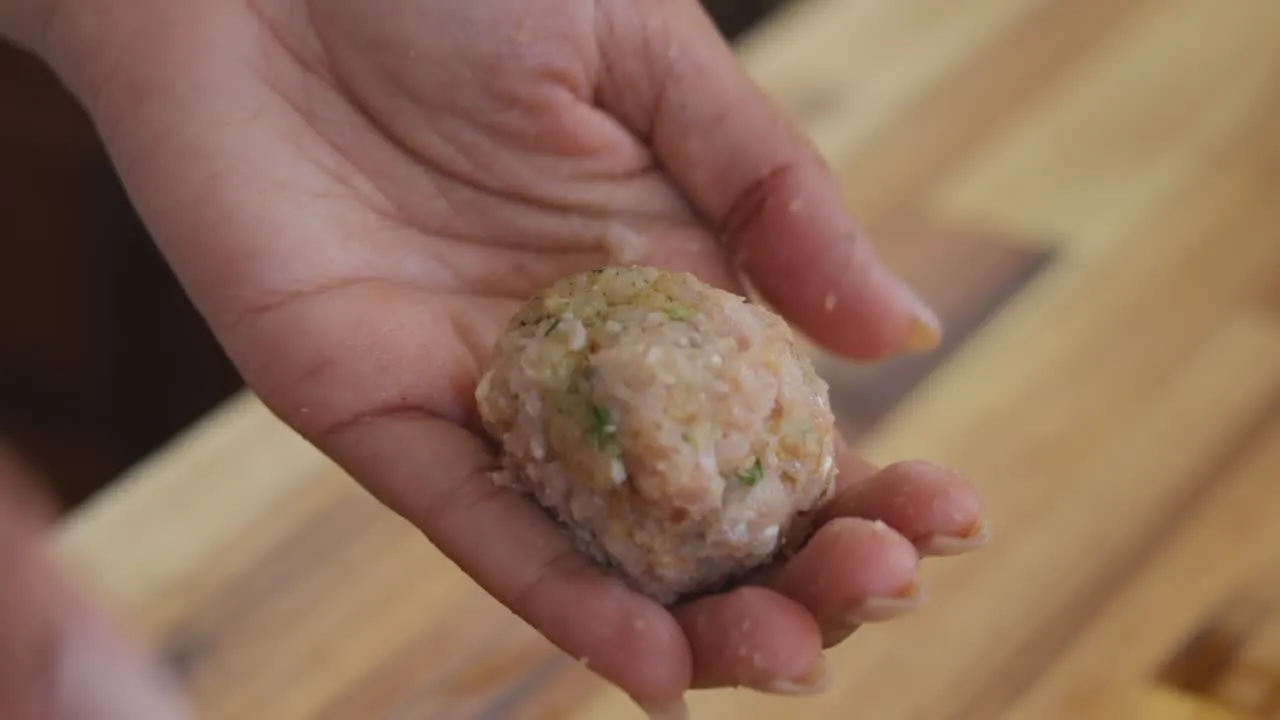 Hand holding seasoned meatball mixture.