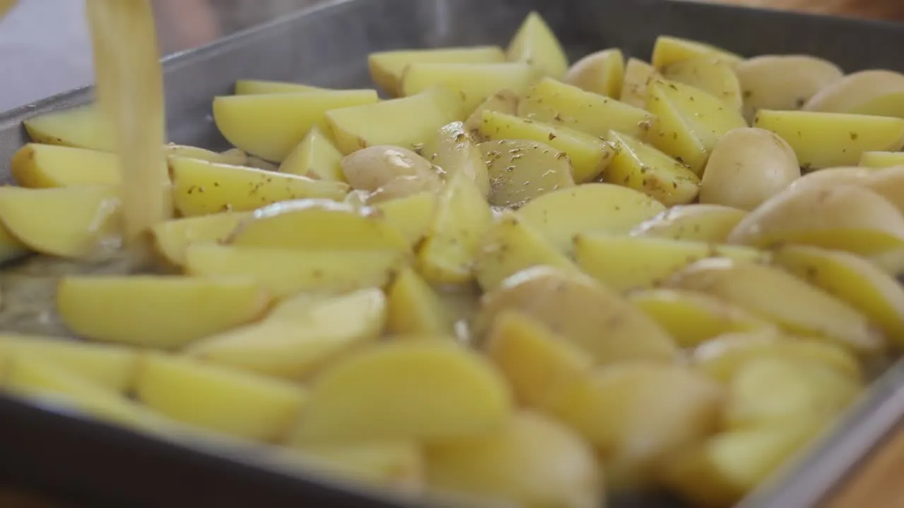 Sliced potatoes being seasoned with dressing on a baking tray.