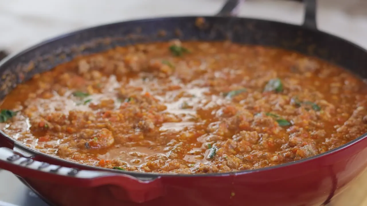 Rich, flavorful Bolognese sauce simmering in a red pan, garnished with fresh herbs.