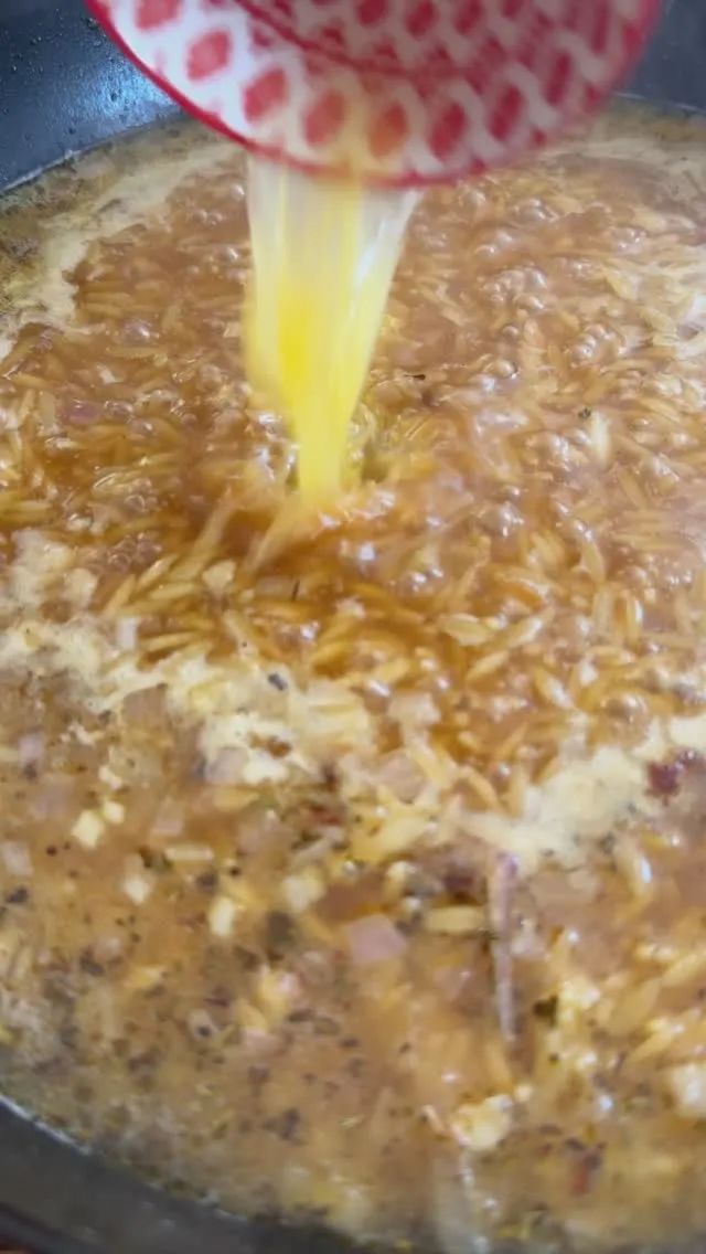 Pouring lemon juice into simmering broth with cooked onions in a pan.