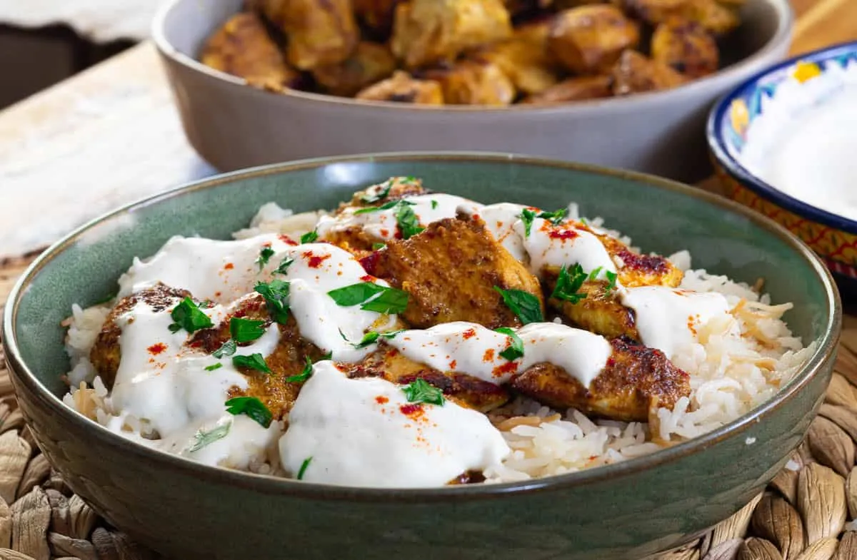 Garlic yogurt marinated chicken kebab with rice and creamy sauce, garnished with parsley, served in a green bowl.