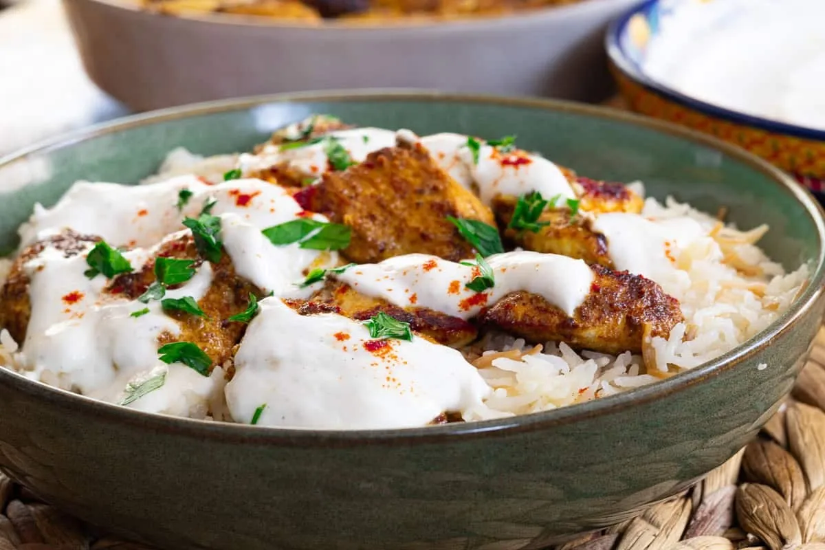 Garlic yogurt marinated chicken kebab with creamy sauce on basmati rice, garnished with fresh herbs in a bowl.