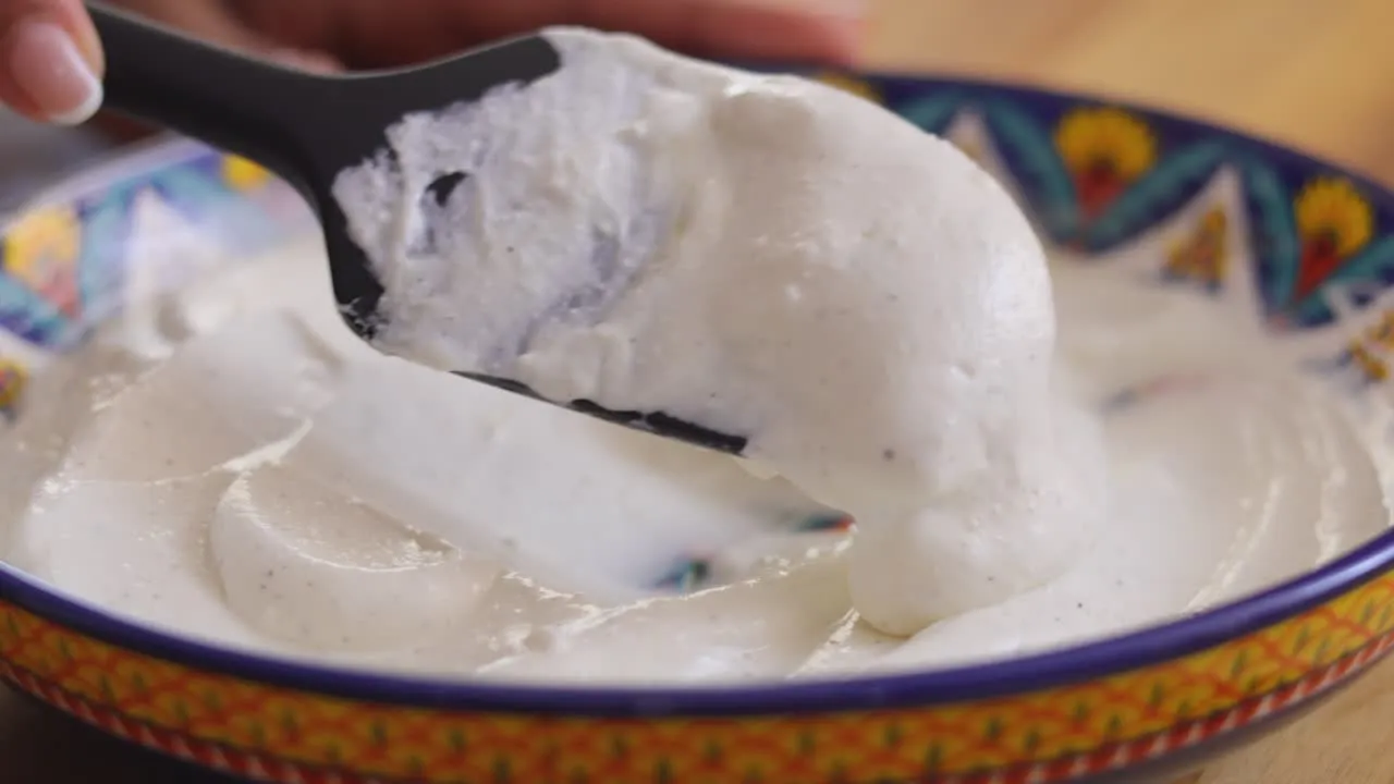 Creamy yogurt being scooped from a colorful bowl with a black spatula.