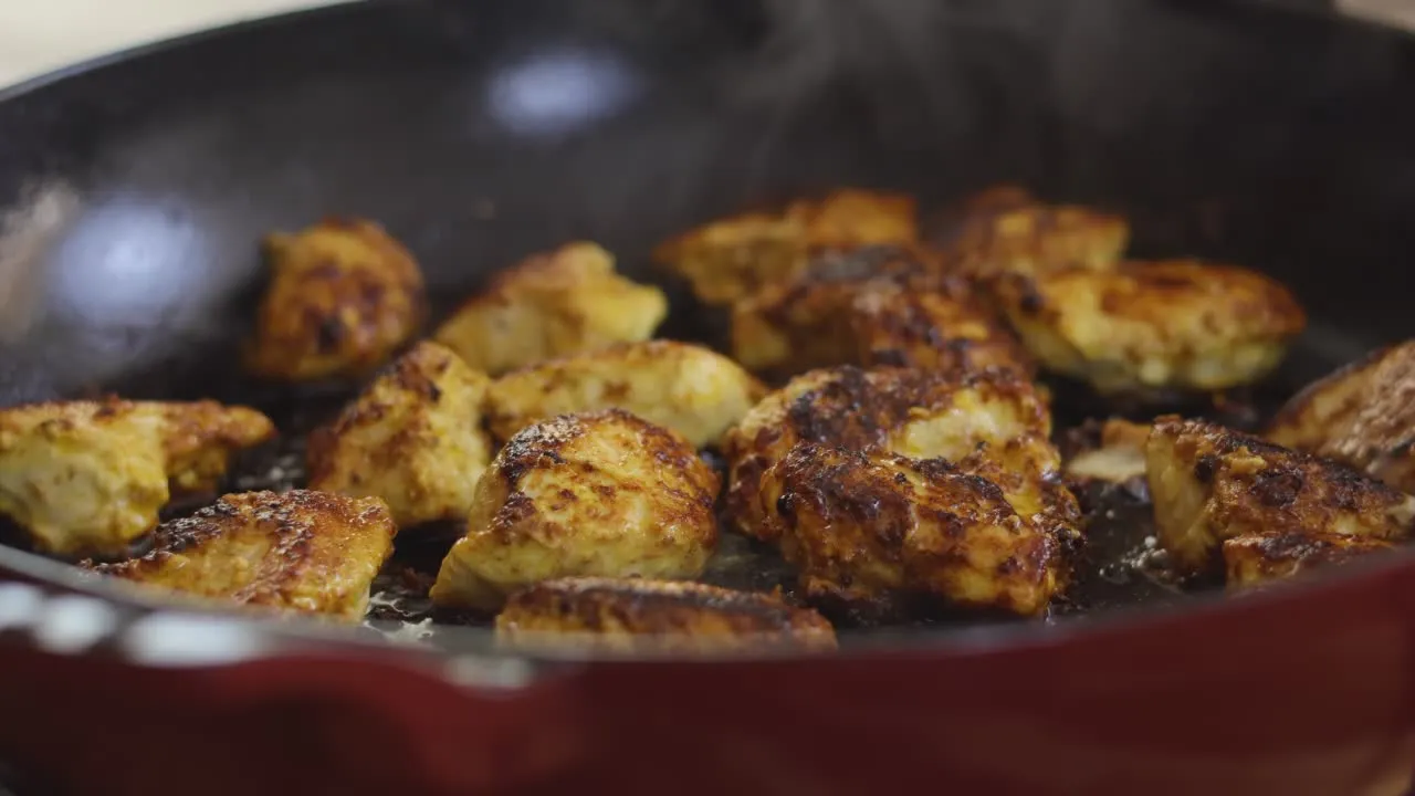 Golden brown chicken pieces sizzling in a pan.