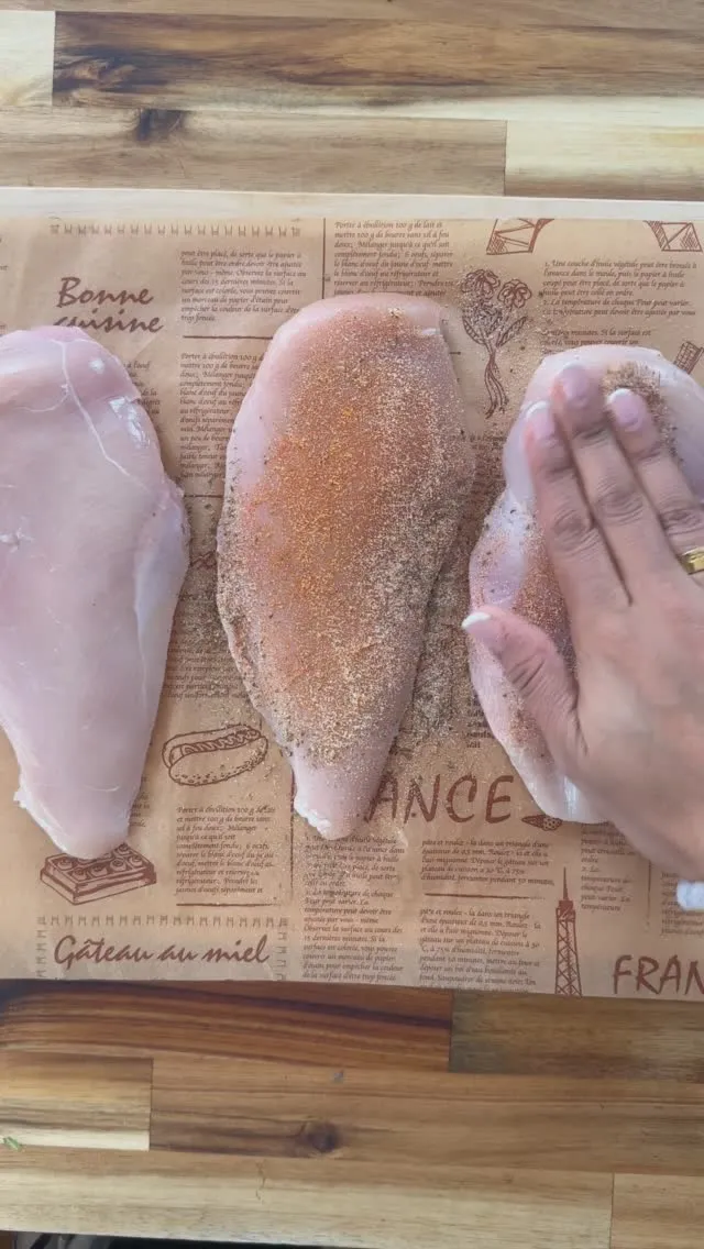 Hand seasoning raw chicken breasts on a rustic wooden cutting board.
