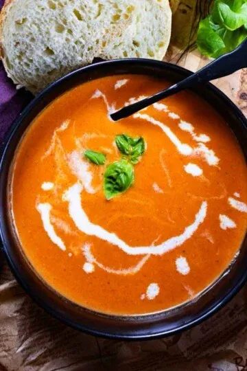 Creamy tomato soup garnished with basil in a black bowl, accompanied by bread slices.