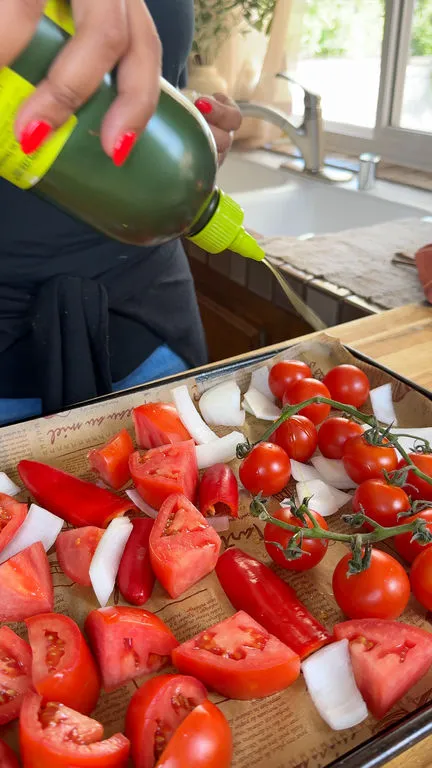 Preparing fresh tomatoes, onions, bell peppers on a baking tray with olive oil drizzle for roasting.