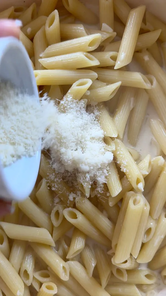Pouring grated cheese onto cooked penne pasta.